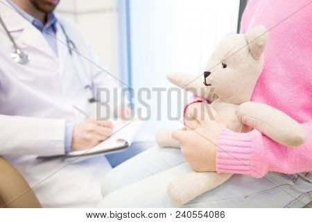 White teddybear in hands of little patient waiting for her doctor making prescriptions