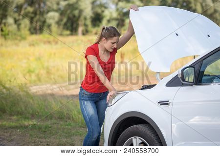 Depressed Woman Looking On The Engine Of Broken Car In Field