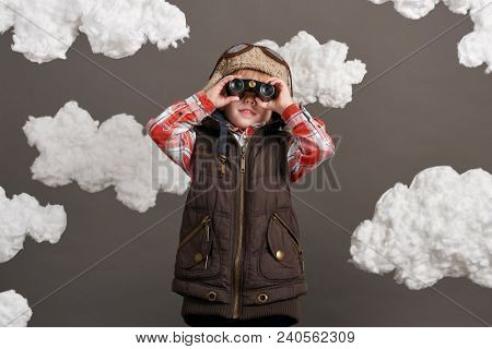 boy dressed as an airplane pilot stands between the clouds and looks through binoculars
