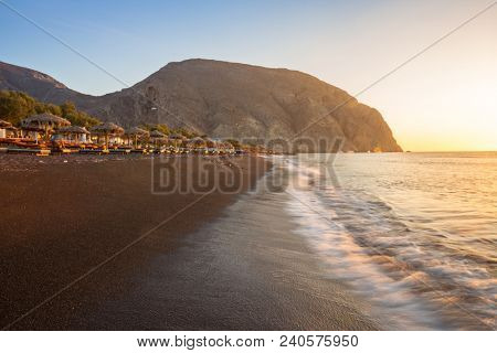 Perissa beach during sunrise on the Greek island of Santorini with sunbeds and umbrellas.