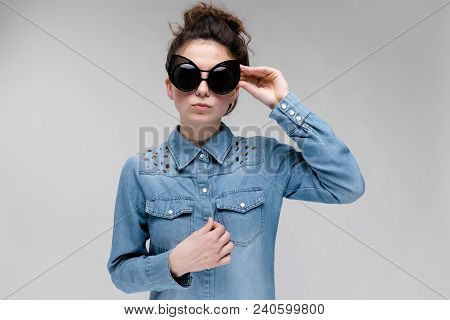 Young Girl In Black Cat Glasses On A Gray Background. Portrait Of A Young Beautiful Girl. Charming G