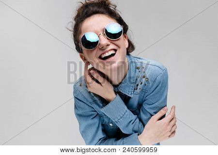Young Girl In Round Glasses On A Gray Background. Portrait Of A Young Beautiful Girl. Charming Girl 