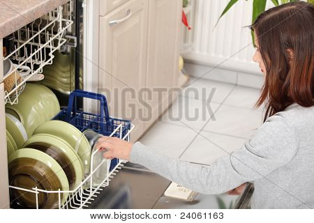 Giovane donna in cucina rassettando. Tirando fuori piatti dalla lavastoviglie