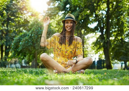 Woman portrait - Happy young woman in the city park outdoor in summer wearing summer dress and trendy hat sitting on grass. Lensflare and vivid colors.