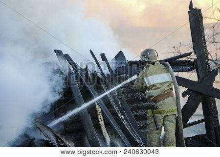 Firefighter Extinguishes The Fire. Fireman Holding A Hose With Water, Watering A Strong Stream Of Bu