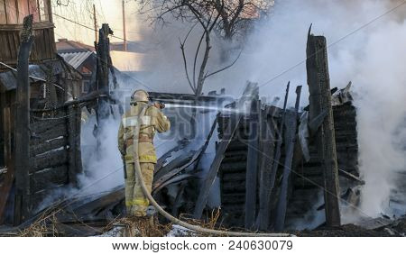 Firefighter Extinguishes The Fire. Fireman Holding A Hose With Water, Watering A Strong Stream Of Bu