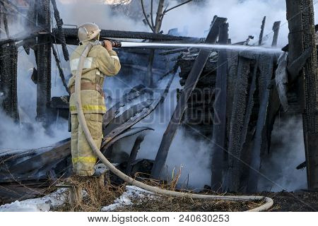 Firefighter Extinguishes The Fire. Fireman Holding A Hose With Water, Watering A Strong Stream Of Bu
