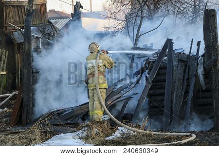 Firefighter Extinguishes The Fire. Fireman Holding A Hose With Water, Watering A Strong Stream Of Bu