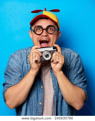 Young Nerd Man With Noob Hat Holding A Vintage Photo Camera On Blue Background