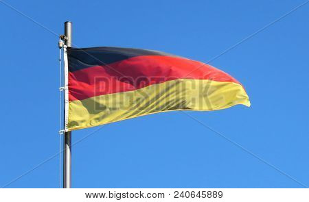 National Flag Of Germany On A Flagpole In Front Of Blue Sky.