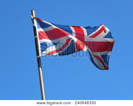 National Flag Of United Kingdom On A Flagpole In Front Of Blue Sky.