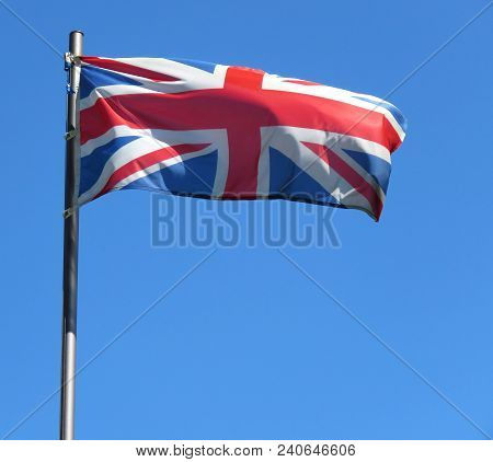 National Flag Of United Kingdom On A Flagpole In Front Of Blue Sky.