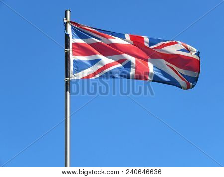 National Flag Of United Kingdom On A Flagpole In Front Of Blue Sky.