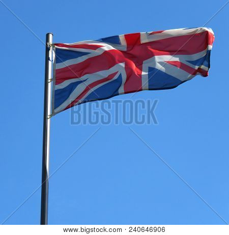 National Flag Of United Kingdom On A Flagpole In Front Of Blue Sky.
