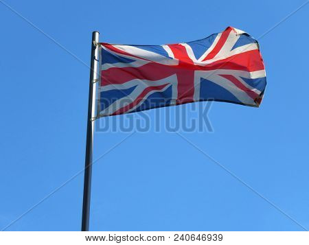 National Flag Of United Kingdom On A Flagpole In Front Of Blue Sky.