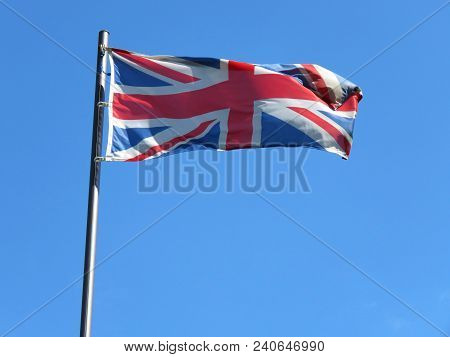 National Flag Of United Kingdom On A Flagpole In Front Of Blue Sky.