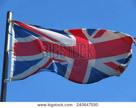 National Flag Of United Kingdom On A Flagpole In Front Of Blue Sky.