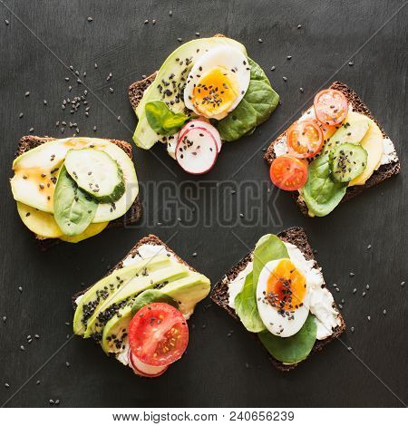 Different Sandwiches With Vegetables, Eggs, Avocado, Tomato, Rye Bread On Black Chalkboard. Top Vew.