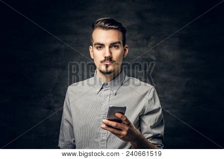 Studio Portrait Of Handsome Bearded Hipster Male With A Tattoo On His Arm Using A Smartphone.