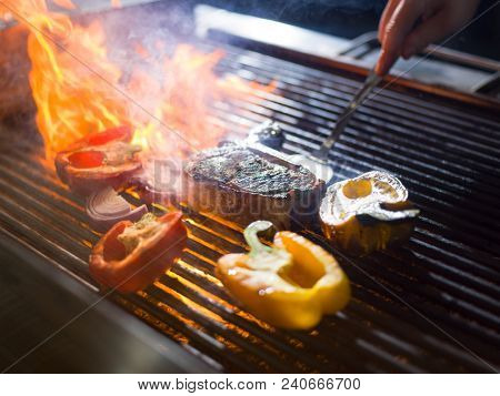 Master chef cooking delicious grilled meat steak with vegetables on a barbecue