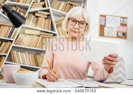 Online Lecture. Attentive Senior Woman Using Tablet While Taking Notes