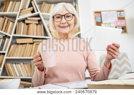Educational Approach. Merry Senior Woman Using Tablet While Drinking Tea