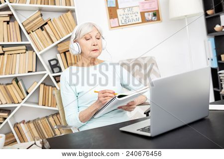 Slower Please. Musing Senior Freelancer Using Laptop While Putting On Headphones