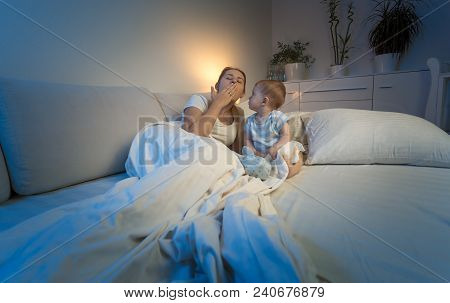 Tired Mother Lying In Bed With Her Baby Boy And Yawning