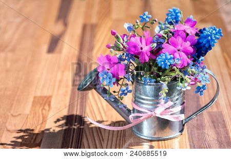 Hyavinth, Forget Me Not And Primose Bouquet In Garden Watering Can With Ribbon Bow On A Wooden Backg