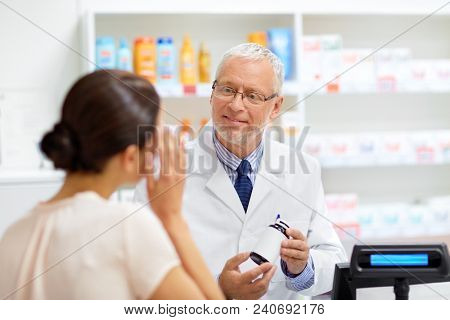 medicine, pharmaceutics, healthcare and people concept - senior apothecary with drug and female customer suffering from headache at pharmacy