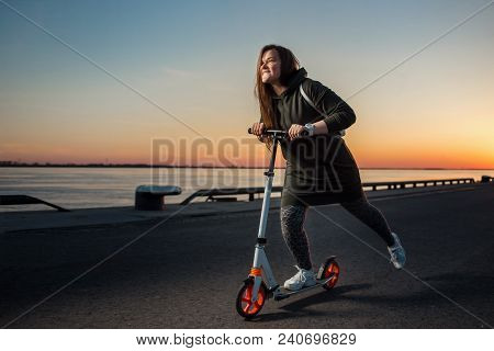 Joyful Woman Quickly Riding A Kick Scooter On Sunset