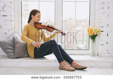 Light Rehearsal. Joyful Brunette Holding Violin While Looking At Strings
