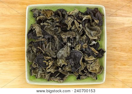 Dried Chinese edible black fungus, called Jew's Ear Mushroom in green dish, top view on wooden background