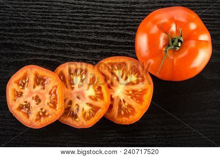 One Red Tomato And Three Slices Top View Isolated On Black Wood Background