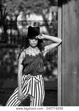 Woman In Stylish Striped Trausers And Black Hat Outdoor Near Green Wooden Door