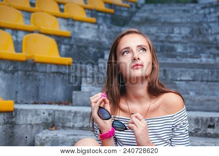 Fashionable Woman With Round Glasses Sitting On The Steps Of The Stadium