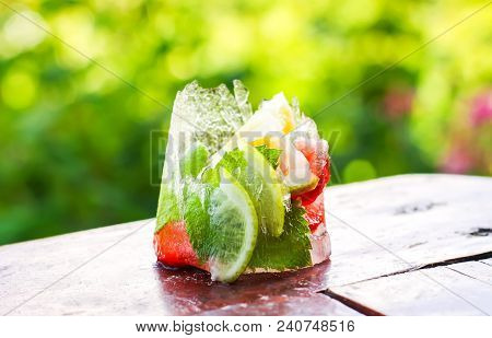 Melting Ice Cube With Strawberry, Lemon And Fresh Green Mint Leaves On Wooden Surface Outdoors