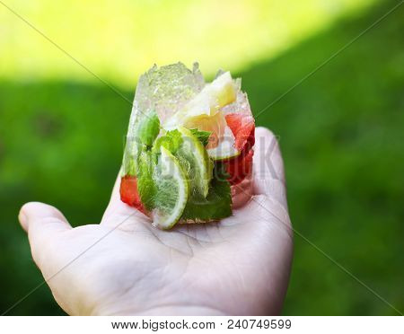 Melting Ice Cube With Strawberry, Lemon And Fresh Green Mint Leaves In A Hand