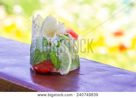 Melting Ice Cube With Strawberry, Lemon And Fresh Green Mint Leaves On Wooden Surface Outdoors