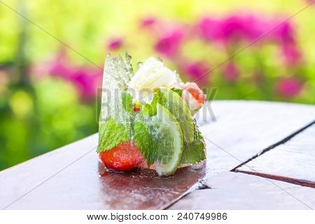 Melting Ice Cube With Strawberry, Lemon And Fresh Green Mint Leaves On Wooden Surface Outdoors
