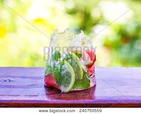 Melting Ice Cube With Strawberry, Lemon And Fresh Green Mint Leaves On Wooden Surface Outdoors