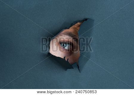 Eye Looking Through Paper. Spy Eye Watching Through A Hole. Eye Looking Through Hole In Black Paper.