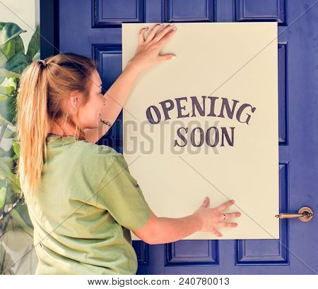 Woman putting on store opening soon sign