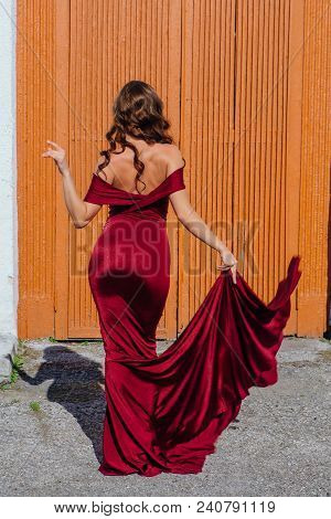 Back View Of A Beautiful Young Woman In A Long Red Evening Gown With A Train Standing Next To The Ol