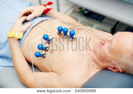 Close-up of calm naked senior male patient with attached soft electrodes making ECG test in clinic to check heart activity