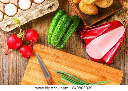 Ingredients For Okroshki - Sausage, Eggs, Radishes, Onions, Potatoes, Cucumbers On An Old Wooden Tab