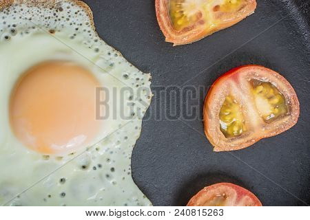 Fried Egg Fried With Chopped Tomatoes In A Cast-iron Frying Pan On A Wooden Table