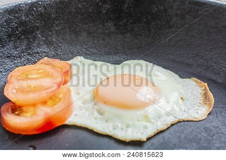 Fried Egg Fried With Chopped Tomatoes In A Cast-iron Frying Pan On A Wooden Table