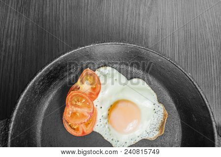 Fried Egg Fried With Chopped Tomatoes In A Cast-iron Frying Pan On A Wooden Table
