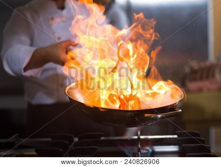 Chef cooking and doing flambe on food in restaurant kitchen